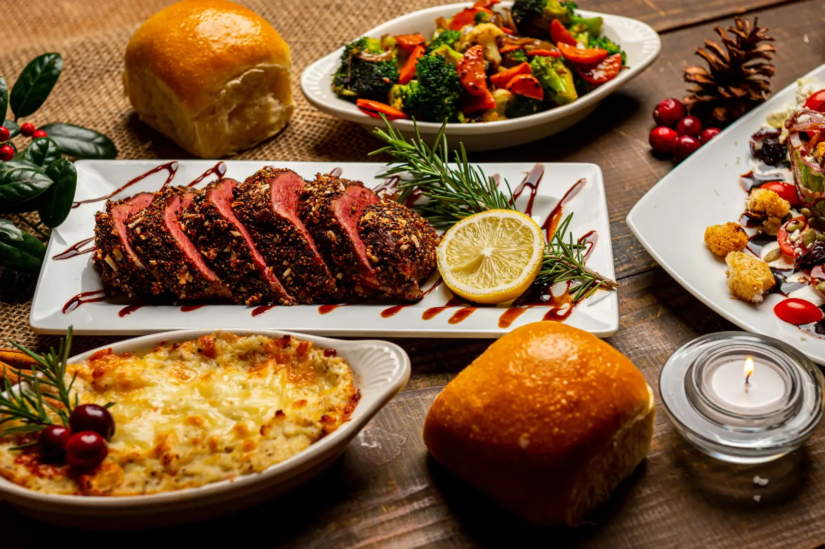Auf dem Foto sieht man eine Holzoberfläche auf der mehrere Gerichte aus Gemüse, Fleisch und als Gratin serviert und schön dekoriert sind.